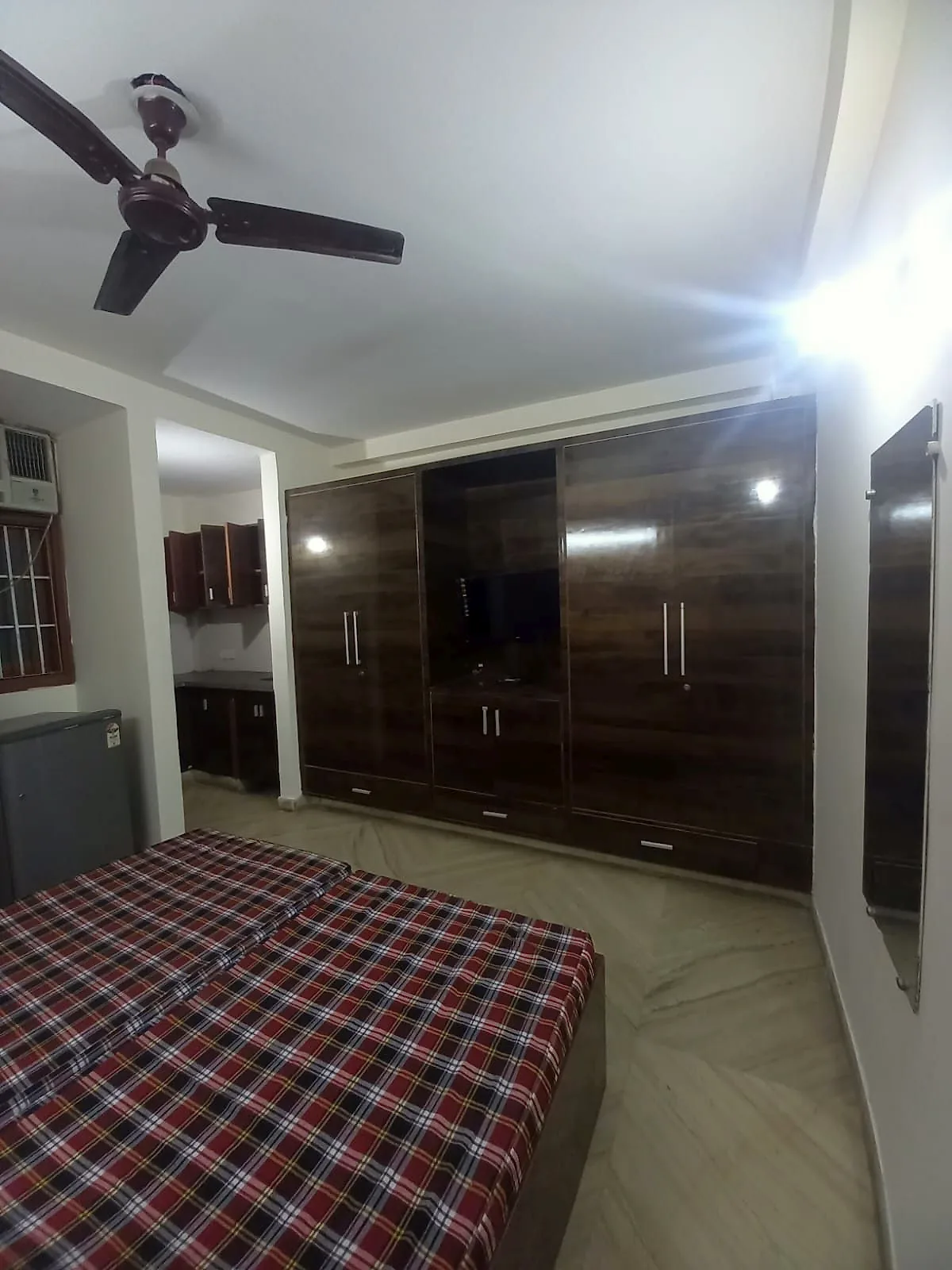 Furnished room with a full-height wardrobe unit, built-in TV niche, air conditioning and kitchen behind