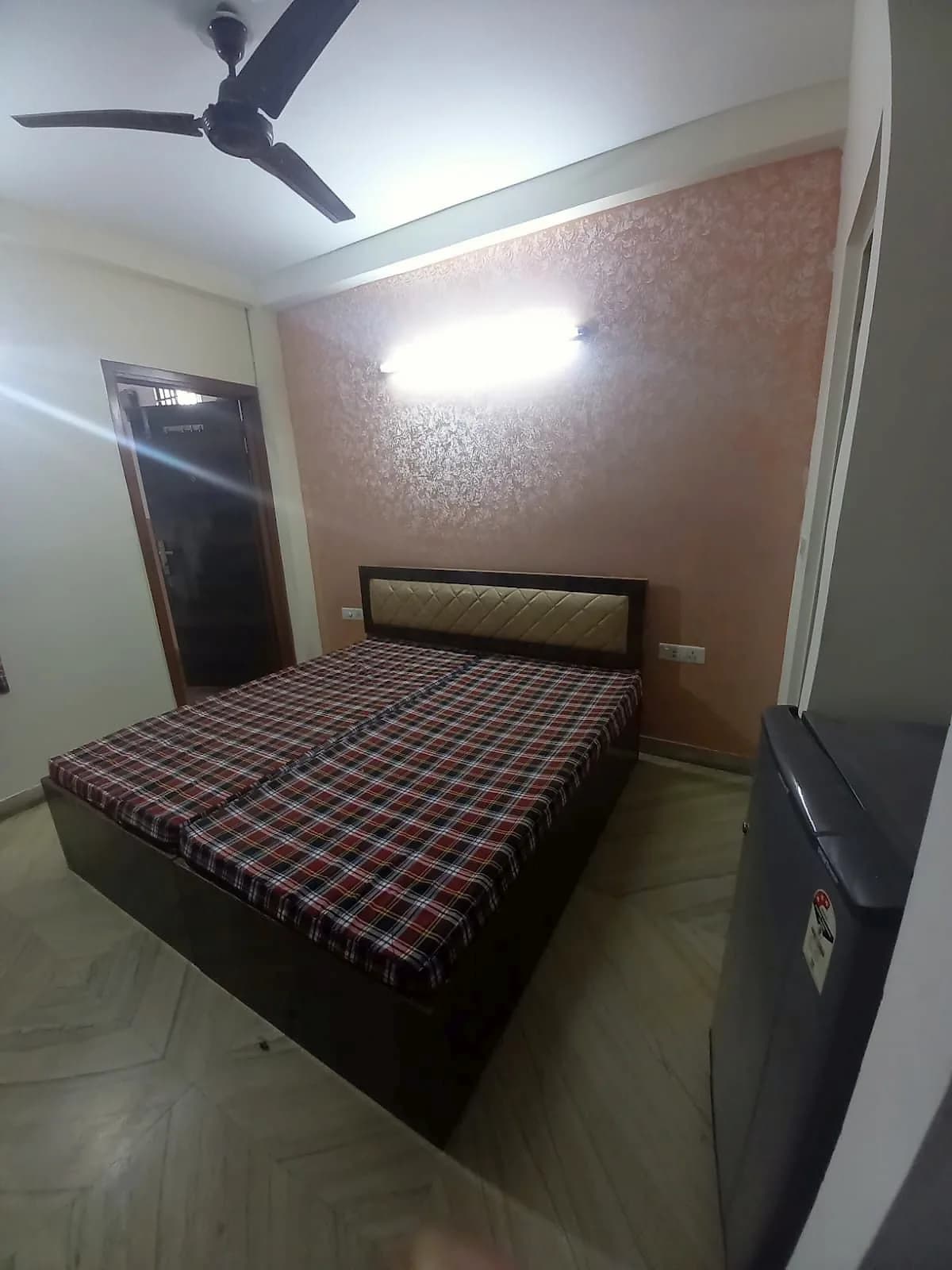 PG room with a cushioned headboard double bed, textured feature wall and refrigerator