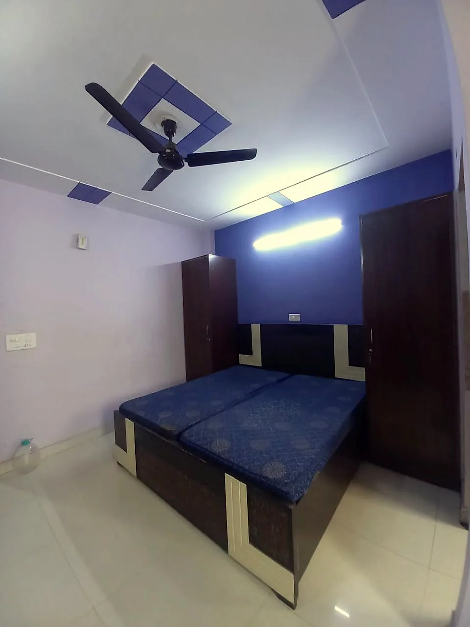 PG room set up for twin sharing with two single beds, wardrobe, ceiling fan and tube light